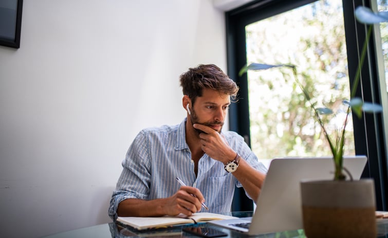 Man in blue shirt sits at laptop by window